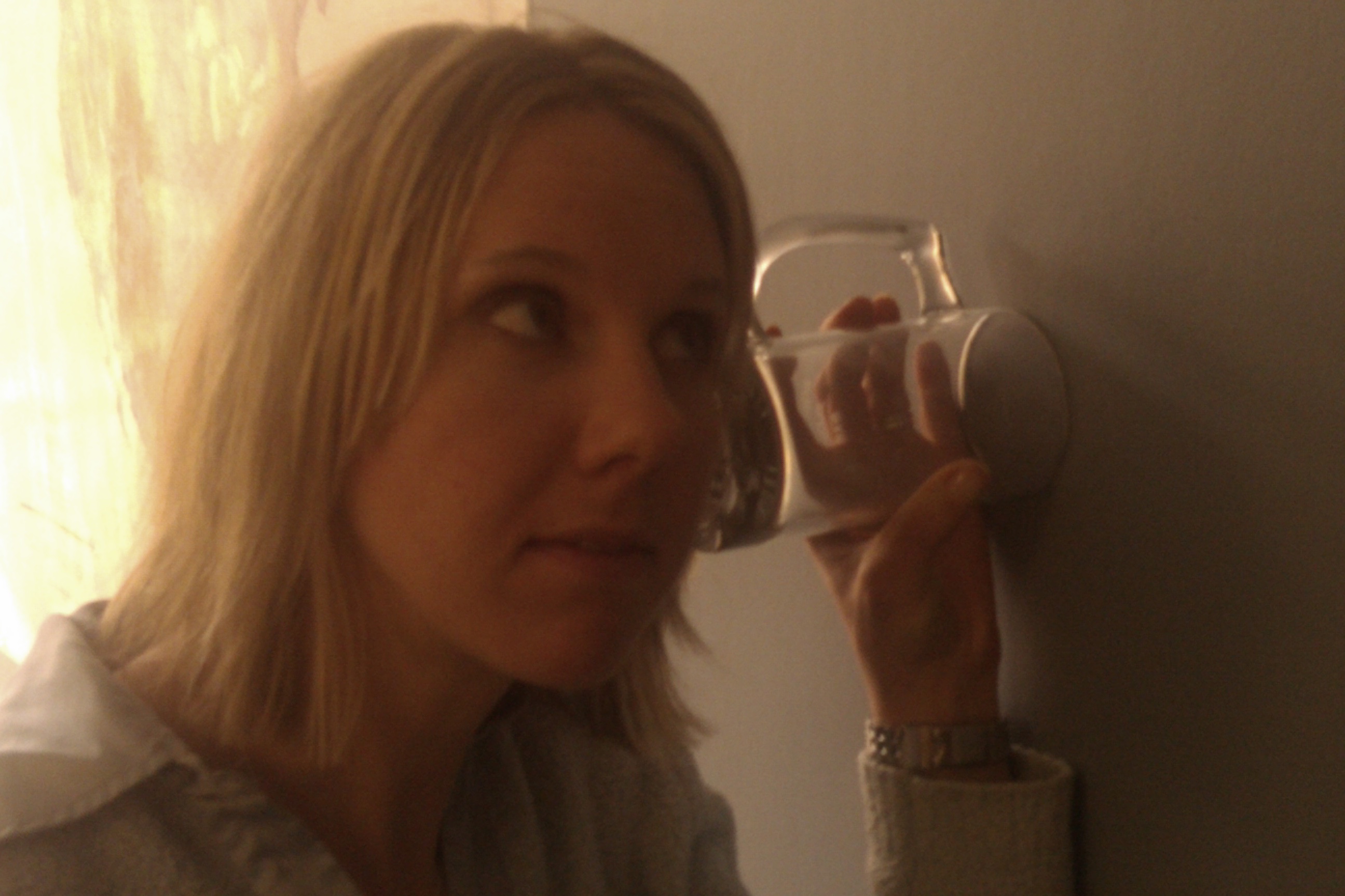 Woman listening for rumors with a jar against the wall