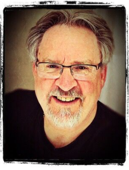 Myk wearing glasses and smiling over his white beard and snazzy black shirt.