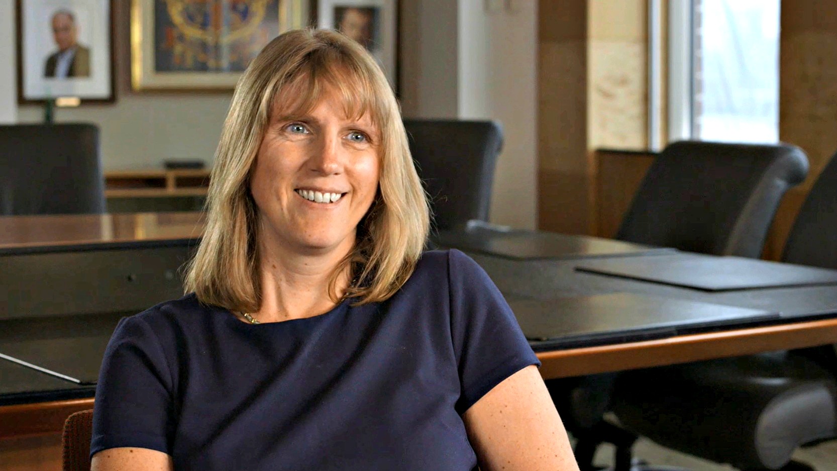 Dr. Polly Smith headshot, image of blond woman smiling in an academic conference room.