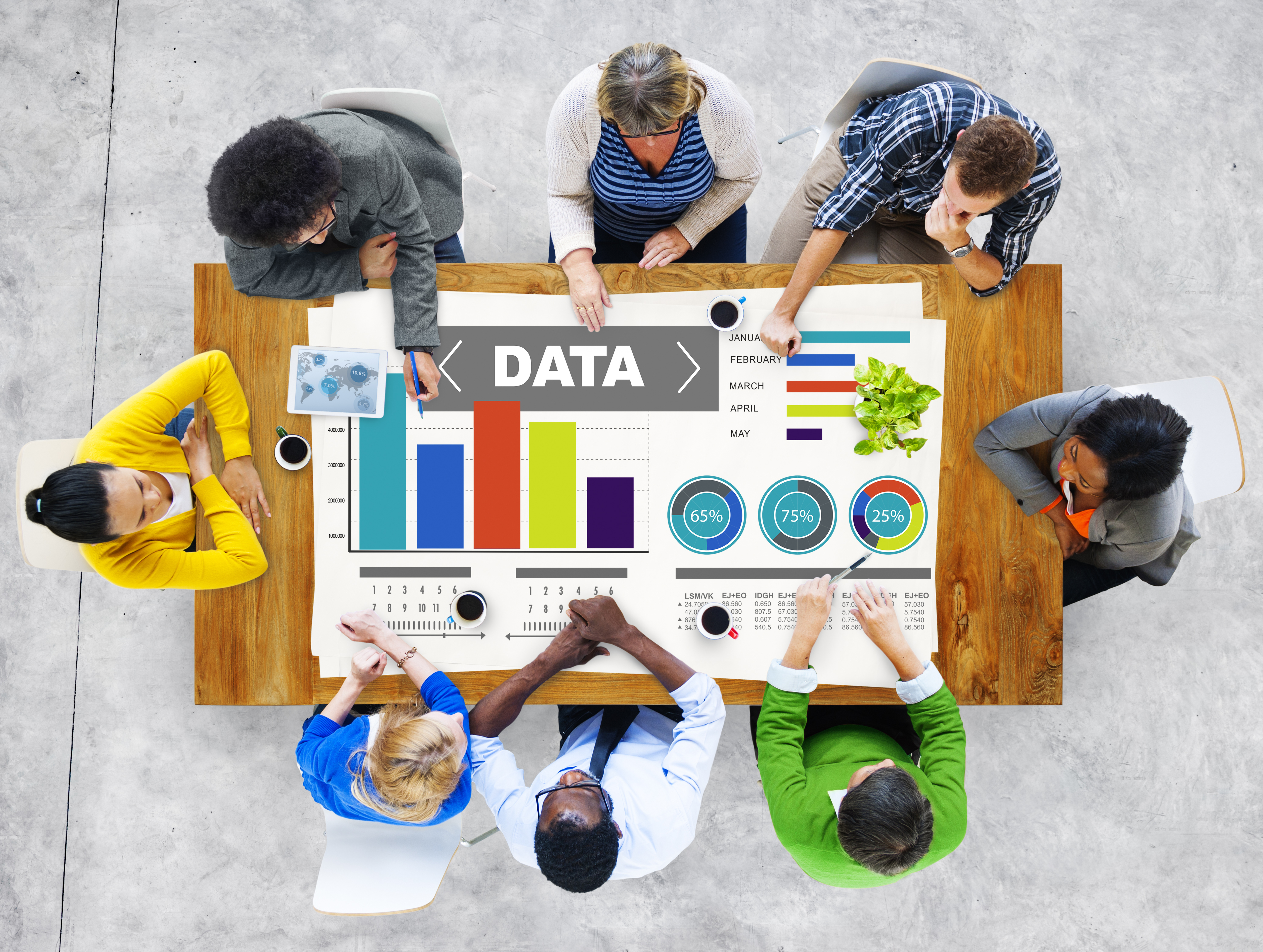 Several people sitting around a table working on a data project. Poster on table reads "DATA" and is surrounded by various charts, graphs. 