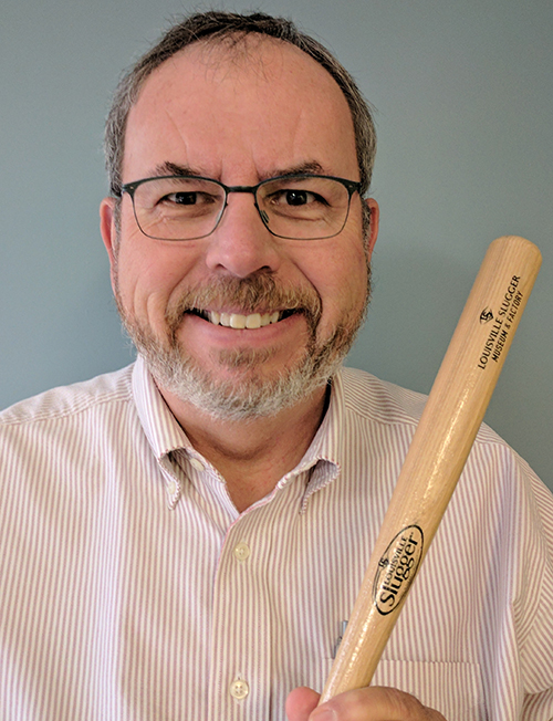 Russ Poulin smiling while holding a small bat