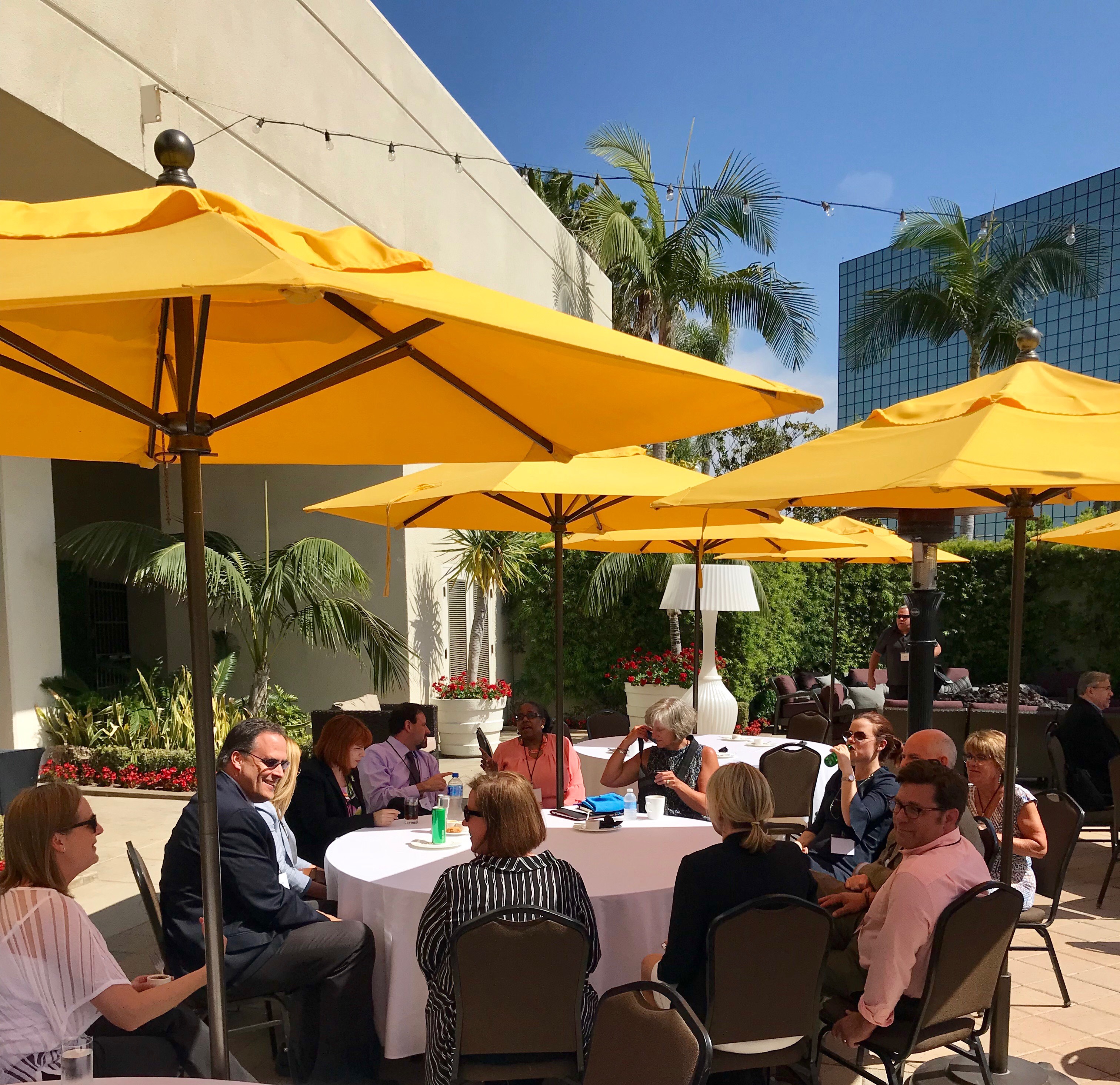 photo of several attendees sitting outside under colorful umbrellas discussing topics.