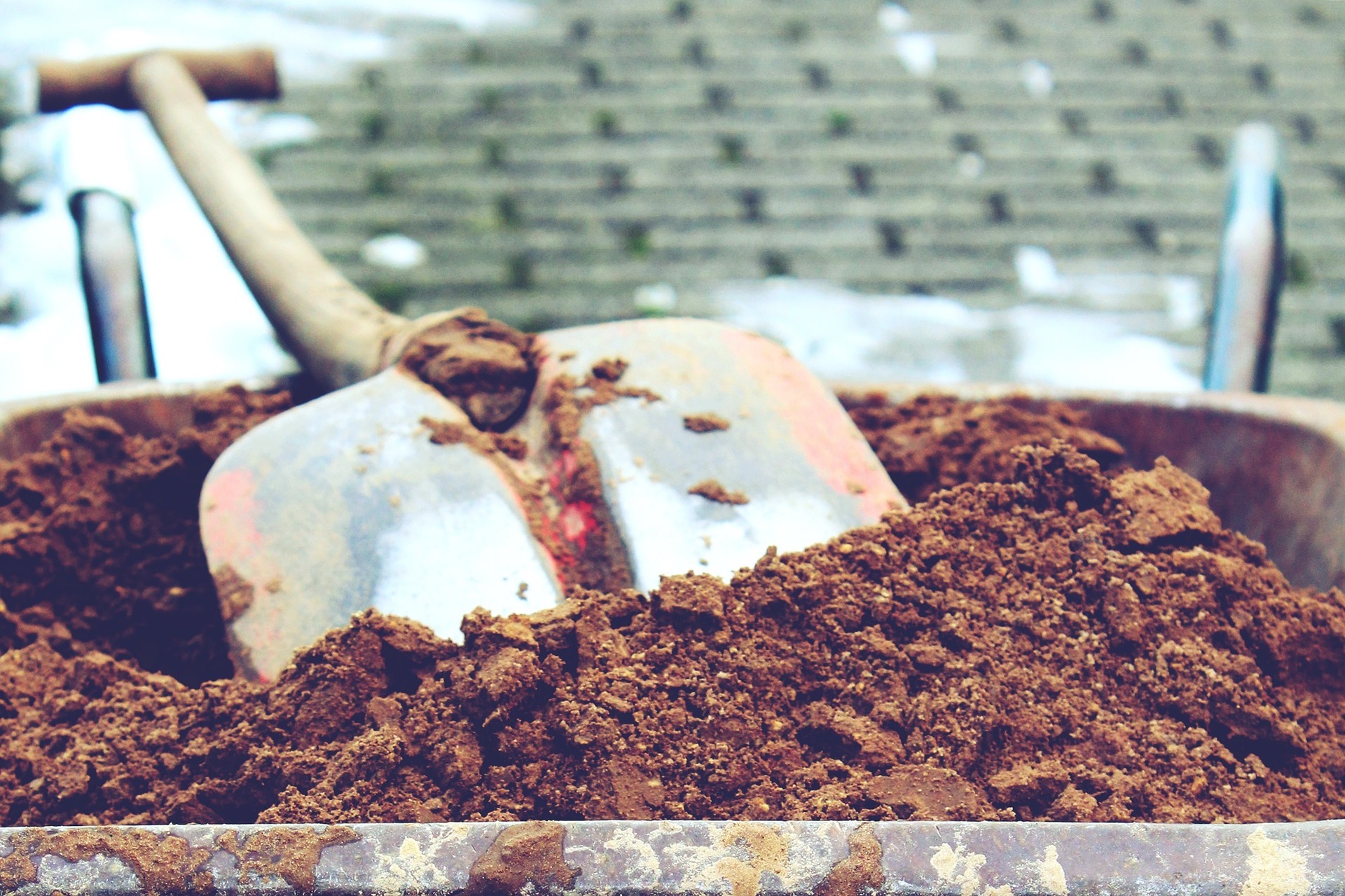 A shovel resting on some dirt in a wheel barrel