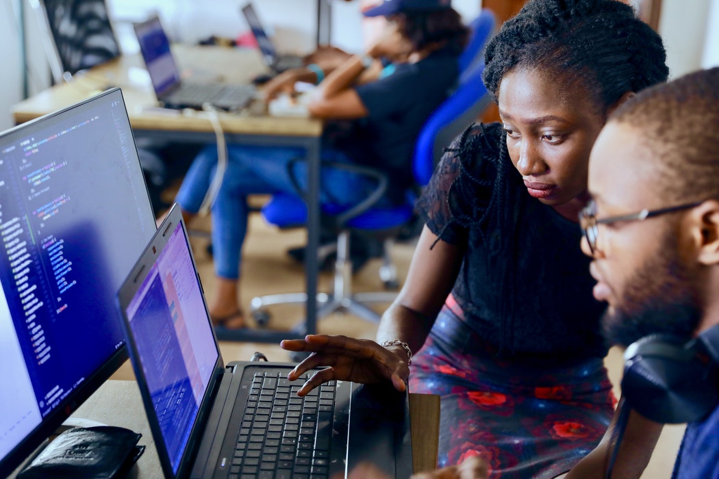 Woman and student looking at two screen of codes. Woman is helping student.