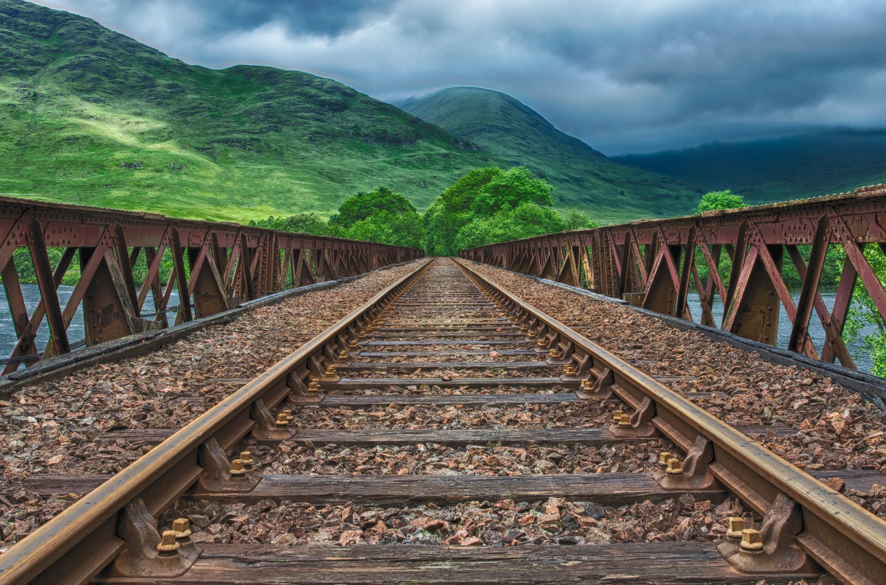 a railroad bridge over water leading toward some trees and mountains