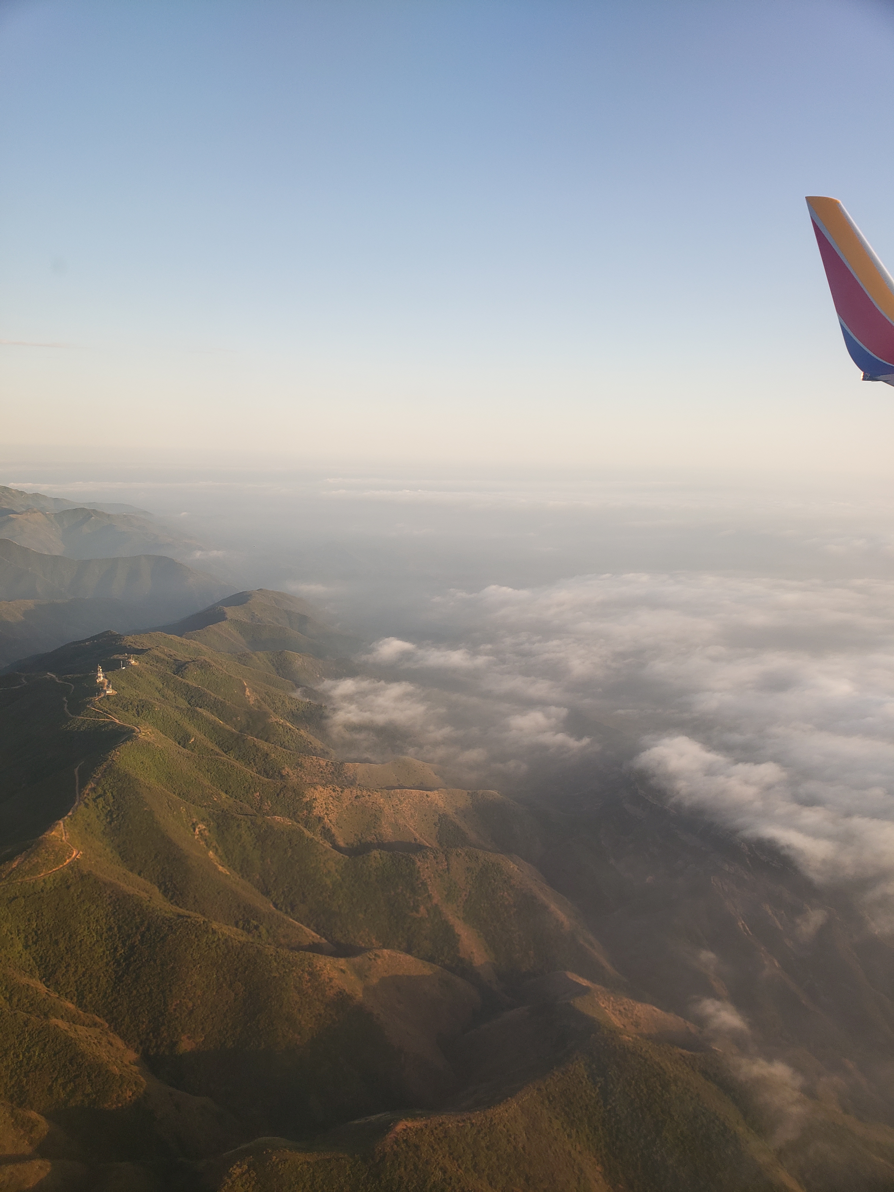 View outside of an airplane window of a mountain range covered in clouds