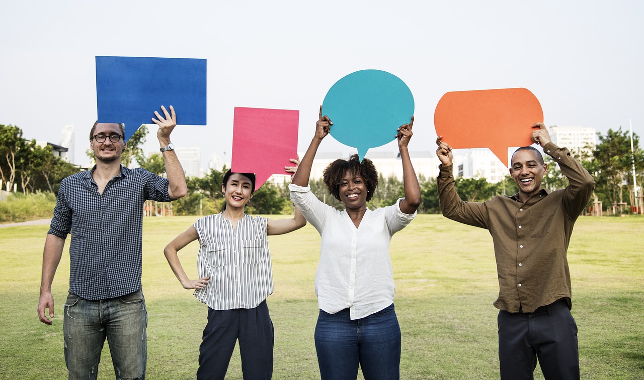 four people holding posters that are shaped like comment bubbles (boxes with arrows pointing at their mouths) indicating that they are commenting