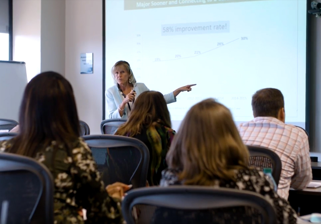 Instructor at front of classroom pointing to a screen