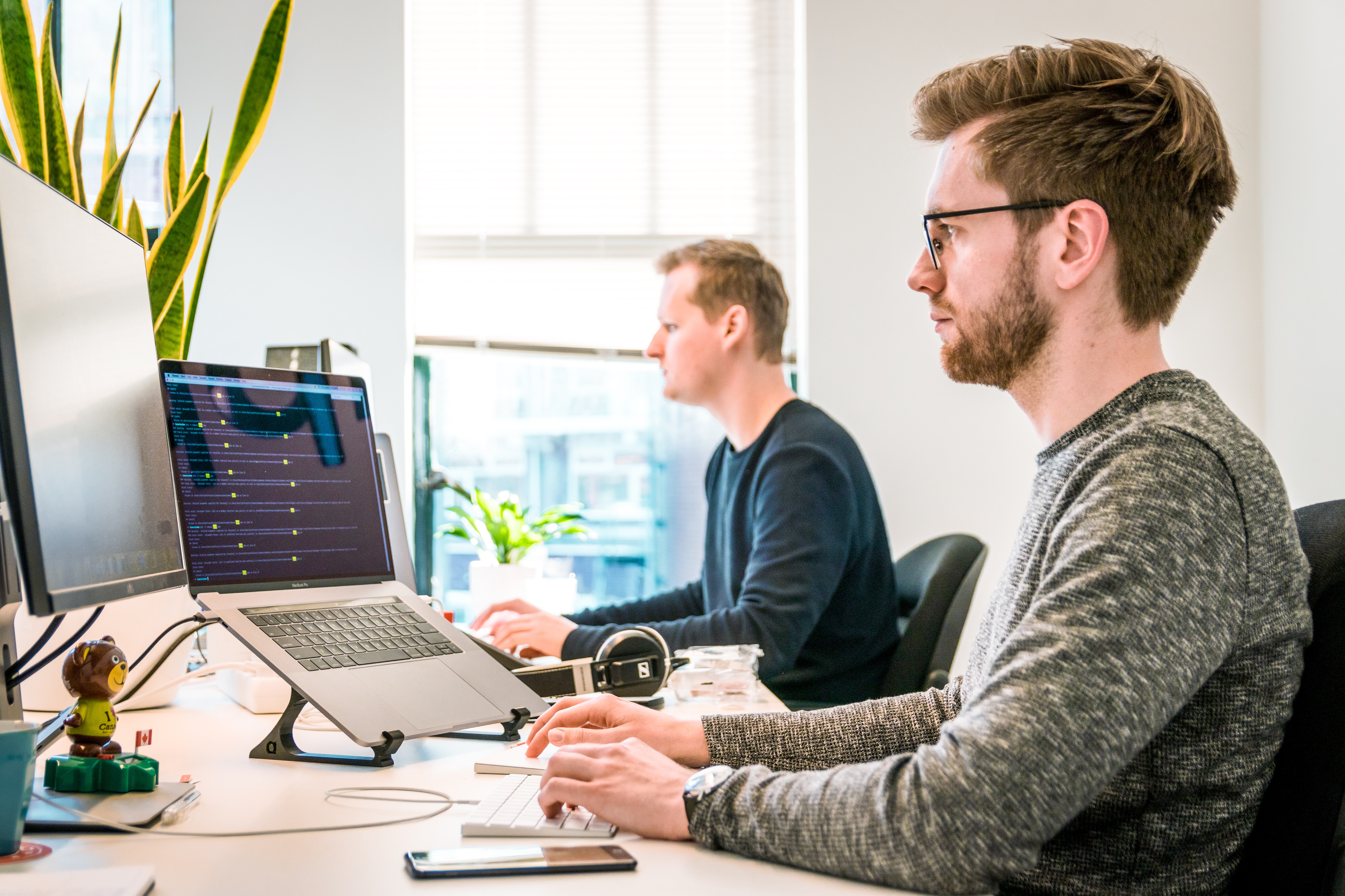 Two white men sitting in an office and writing code at computers.