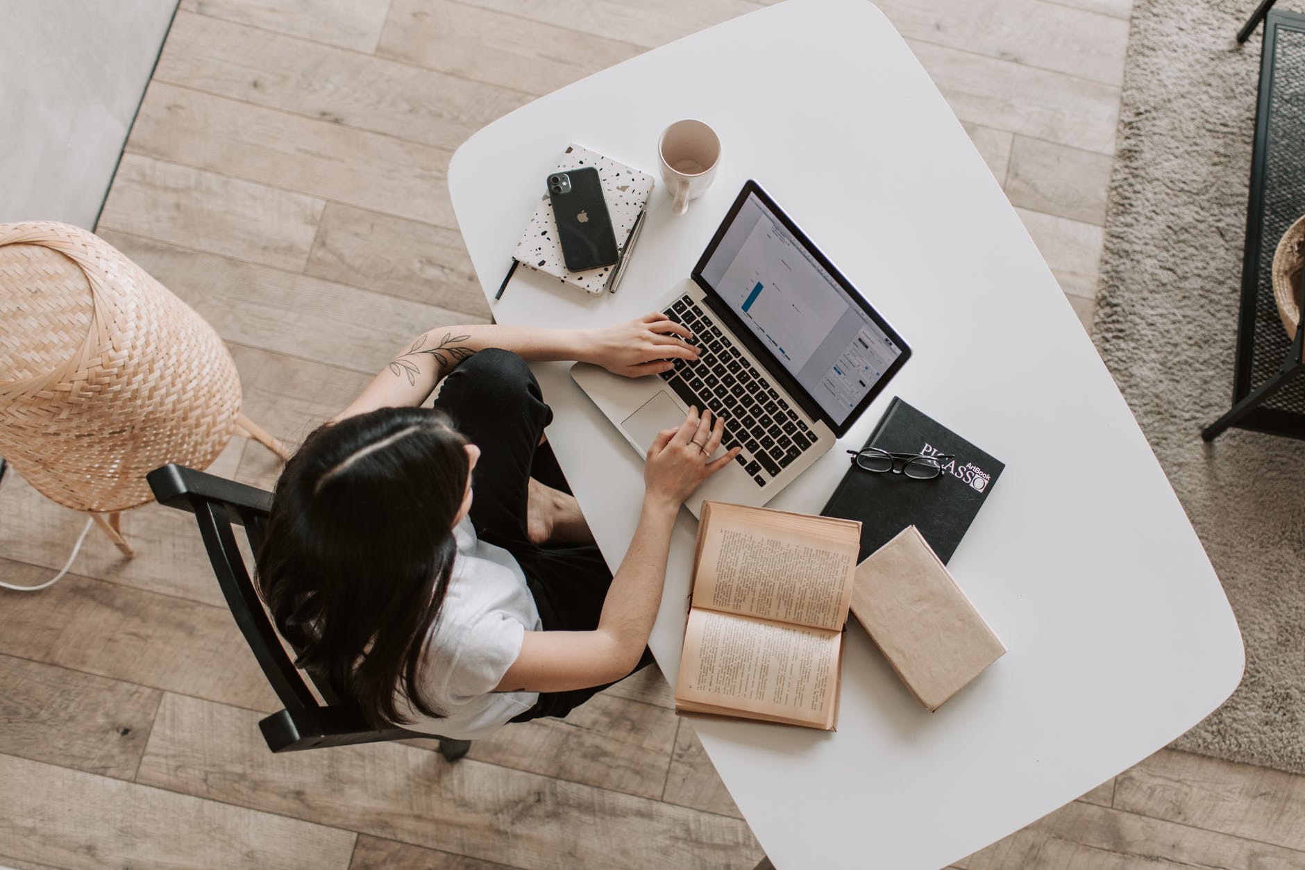 overhead photo of a woman working on a laptop with a book next to her