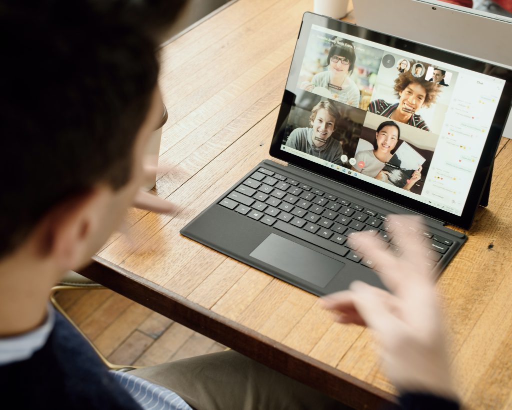 a person gesturing in front of a laptop with several others attending a video call