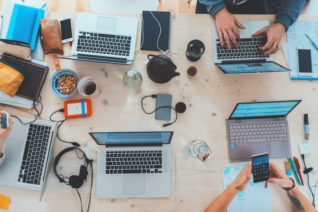 people sitting at a table with several different devices, including laptops and smartphones. 