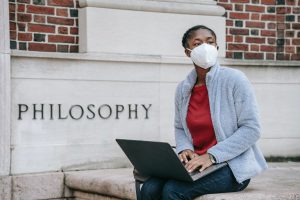 Young woman looking away while typing on laptop near university