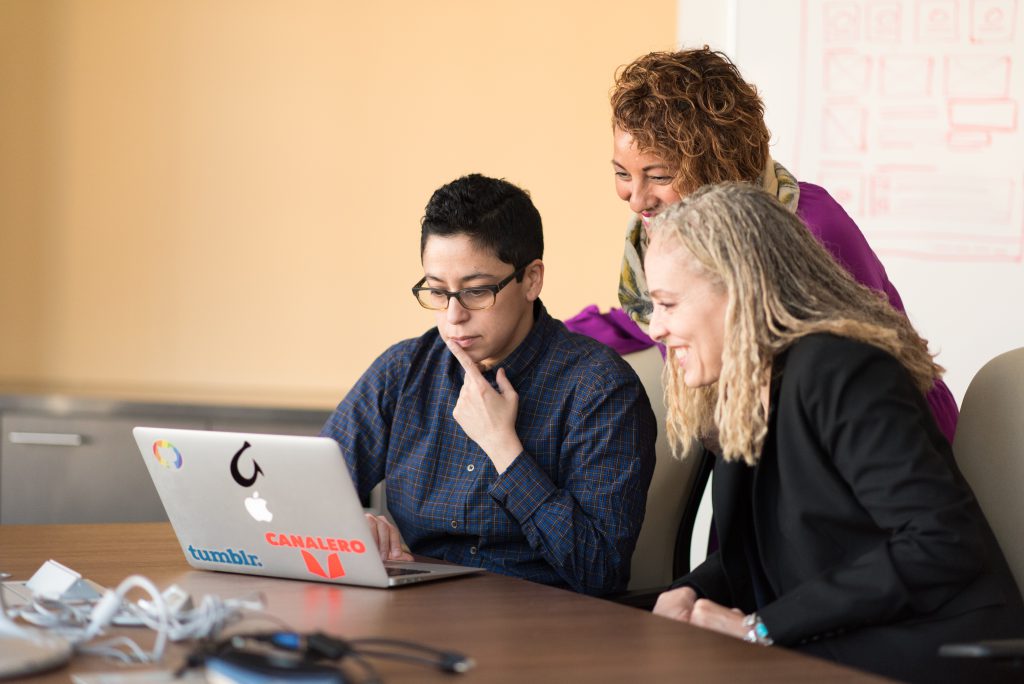 three people look together at a computer