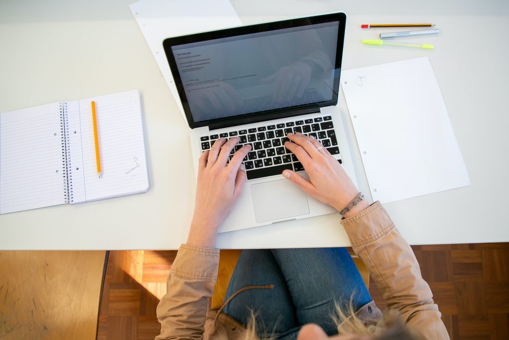 a person sitting at a table typing on a laptop keyboard