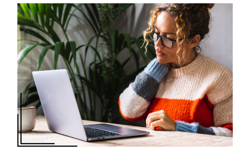 A college-aged woman sitting at a table looking at a laptop